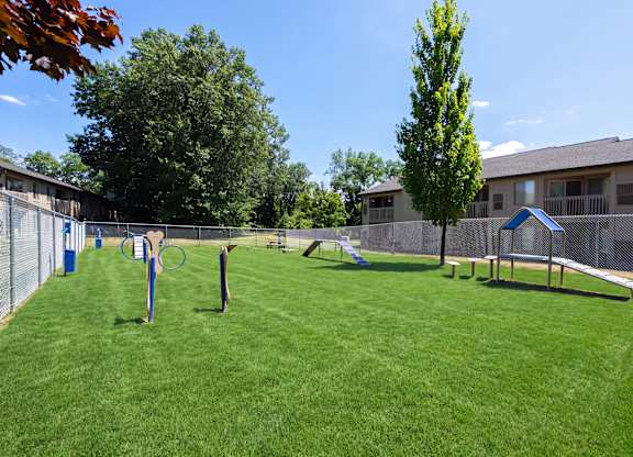 A grassy area with a tennis court and a building in the background.