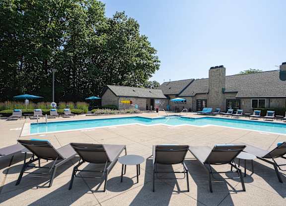 A pool surrounded by chairs and umbrellas with a building in the background.