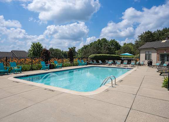 A swimming pool surrounded by blue chairs and a fence.