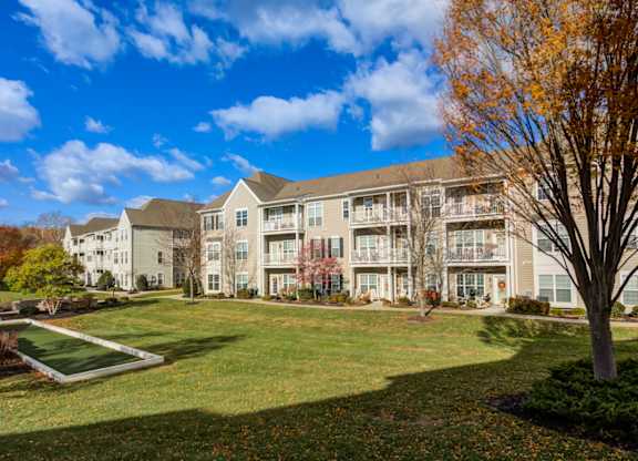 A large apartment complex with a green lawn and trees in the foreground at Meridian West Shore, Pennsylvania 17055