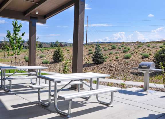 Picnic tables are set up on a patio with a view of a field.