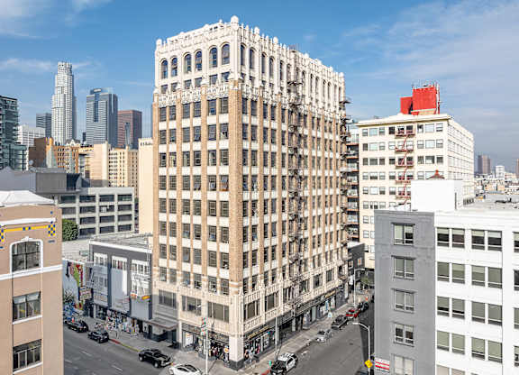 A tall building with many windows is in the middle of a city street.