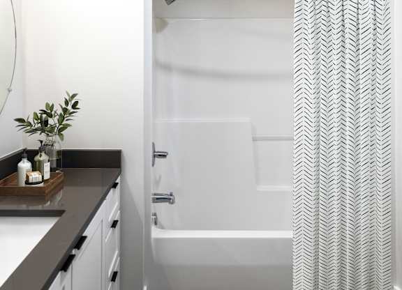A bathroom with a white tub and a grey and white patterned shower curtain.