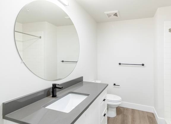 A bathroom with a round mirror, sink, toilet and a shower.