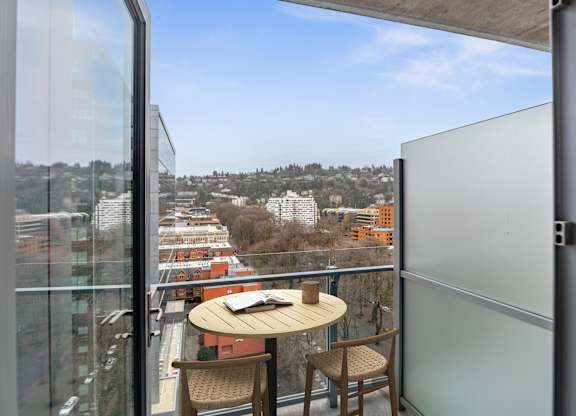 A balcony with a table and chairs overlooking a cityscape.