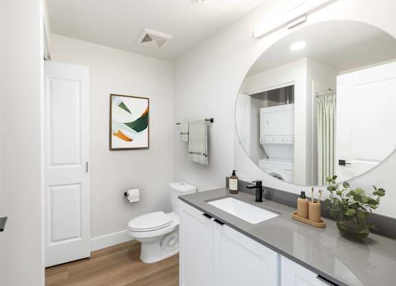 A bathroom with a toilet, sink, mirror, and a painting on the wall.