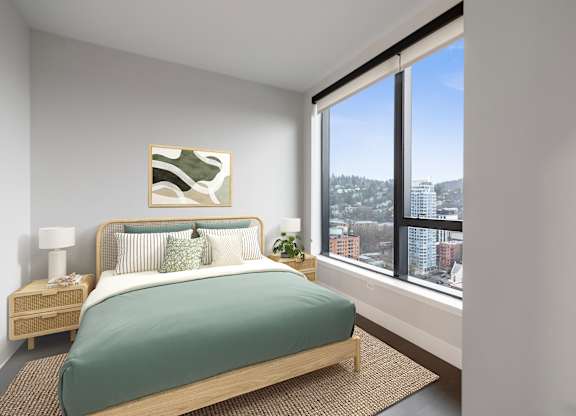 A bedroom with a bed, nightstand, and a window overlooking a cityscape.