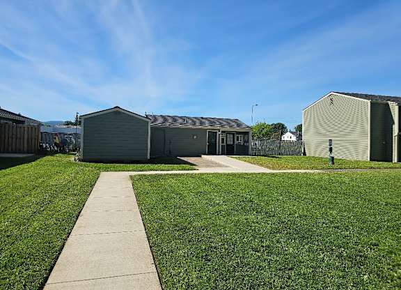 A grassy area with a concrete walkway leading to a building with a grey roof.