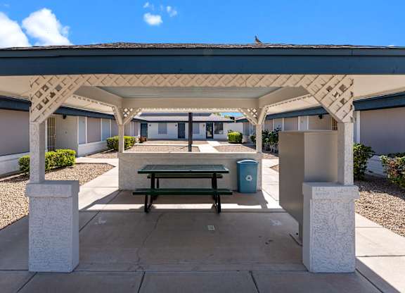 A covered patio area with a bench and a trash can.