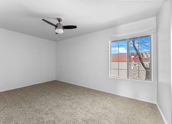 A room with a ceiling fan and a window showing a view of a building and trees.
