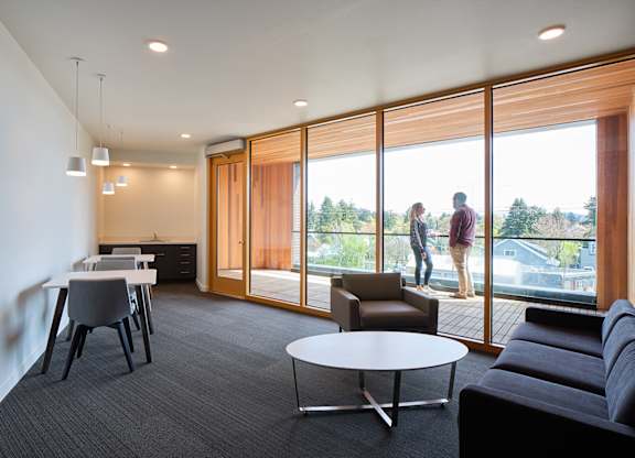 A modern living room with a grey carpet and a large window overlooking a green landscape.