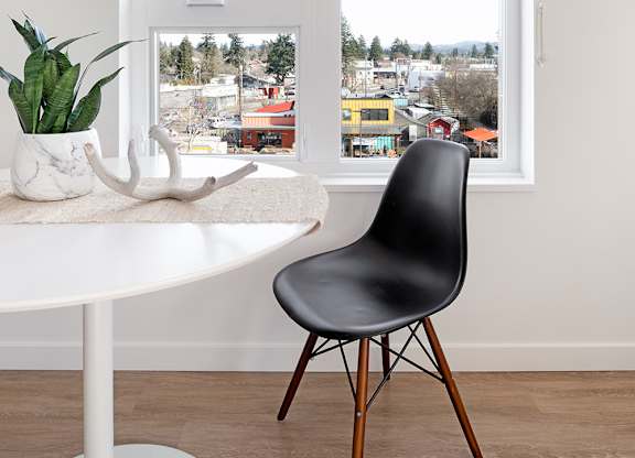A white table with a plant and a chair in front of a window.