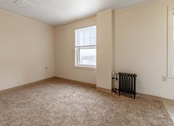 A room with a carpeted floor, a window, and a radiator.