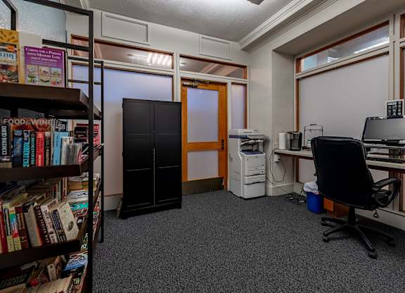 A room with a bookshelf, a desk with a computer, and a black office chair.