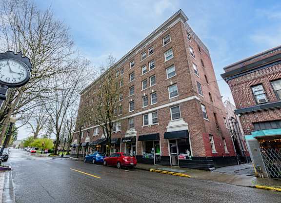 A street view of a brick building with a clock on a pole.