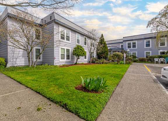 A grey house with a green lawn and a white car parked in front.