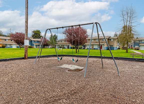 A playground with a swing set in the foreground and apartment buildings in the background.