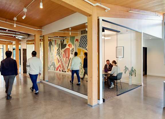 People walking in a hallway with a large painting on the wall.
