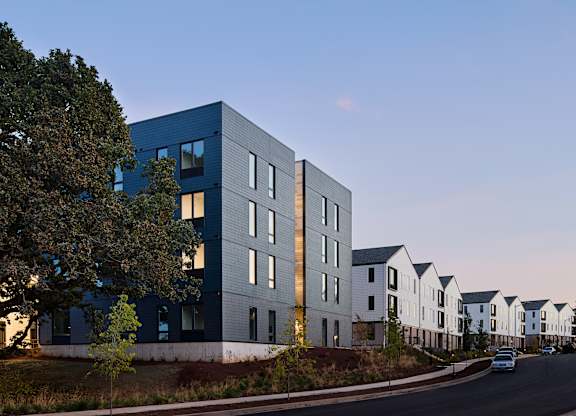 A modern building with a blue facade is situated next to a row of white houses.