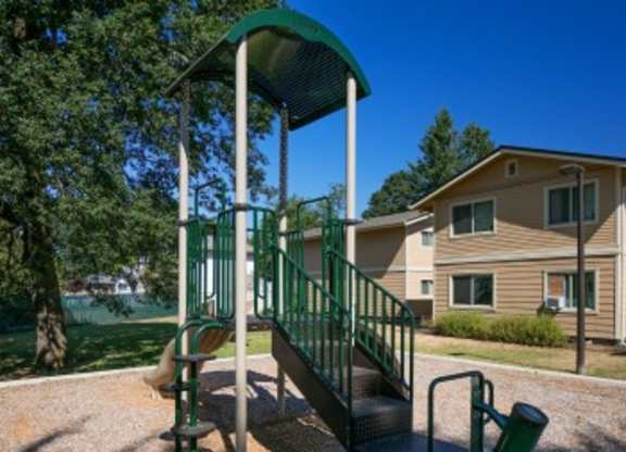 A playground structure with a green canopy and a metal railing is in front of a building.