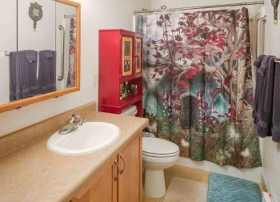 A bathroom with a red cabinet and a shower curtain with a tree design.