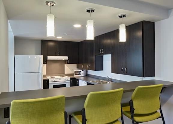 A modern kitchen with a white refrigerator, black cabinets, and green chairs.