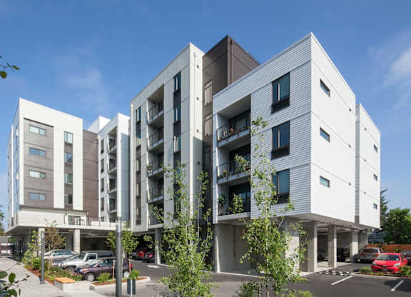 A modern building with white and grey exterior and a parking lot in front.