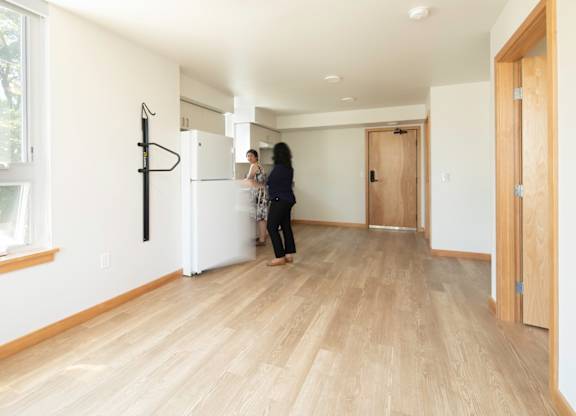 A woman is standing in a room with wooden floors and white walls.