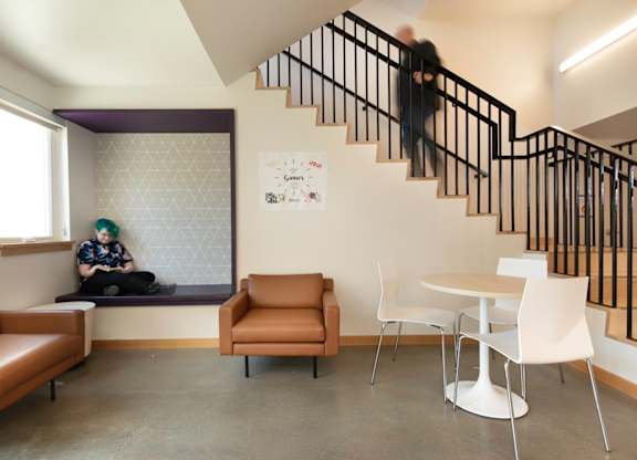A person is sitting on a bench in a room with a staircase.