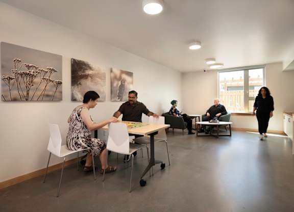 A group of people are sitting around a table in a room with artwork on the wall.