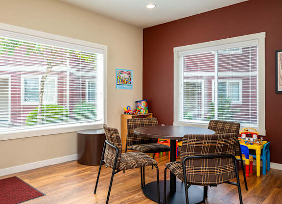 A room with a table and chairs and a window with blinds.