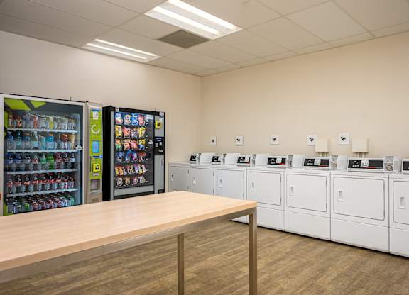 A room with a row of washing machines and a wooden table in front of them.