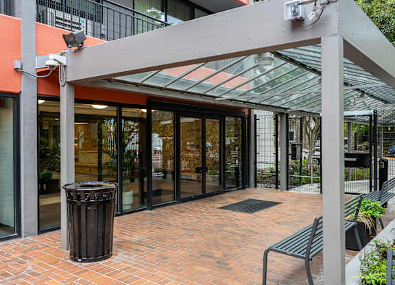 A glass door entrance to a building with a trash can and benches outside.