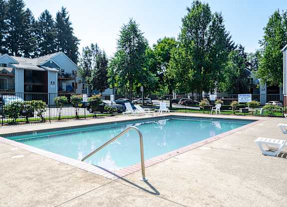 A swimming pool surrounded by trees and a building in the background.