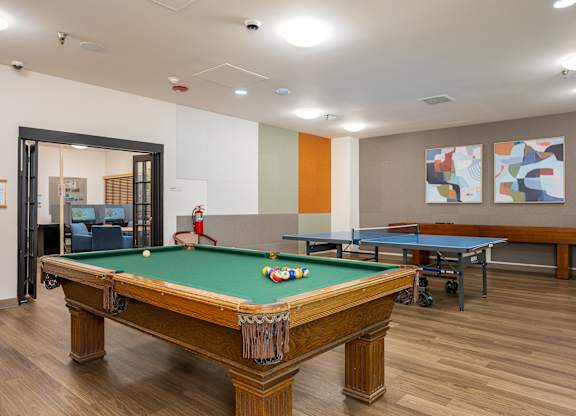 A pool table in a room with a ping pong table and two paintings on the wall.