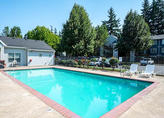A swimming pool surrounded by a concrete patio and a black fence.