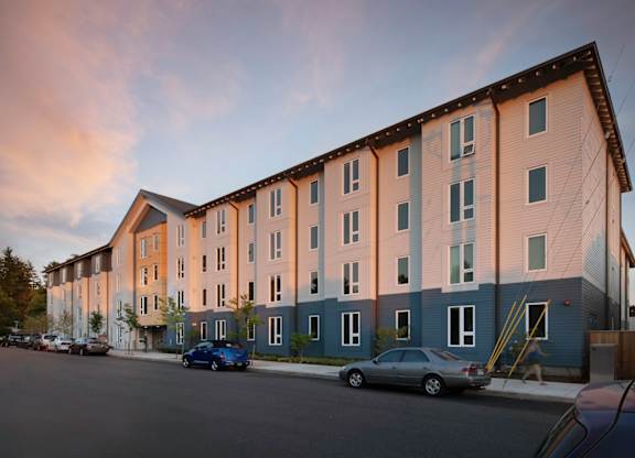 A row of modern apartment buildings with cars parked in front.