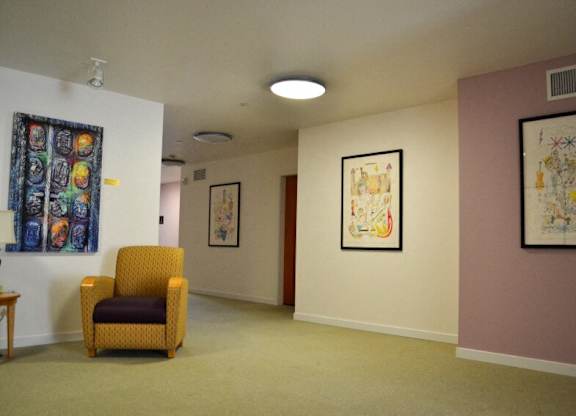 A yellow chair sits in a room with two paintings on the wall.