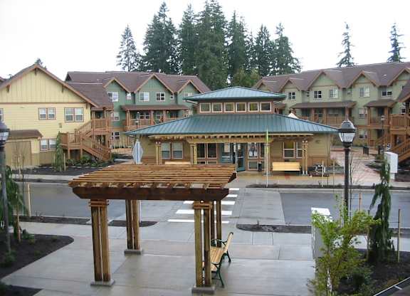 A wooden pavilion with a green roof is in the middle of a courtyard.