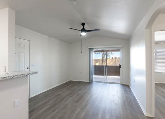 A spacious room with a ceiling fan and sliding glass doors leading to a balcony.