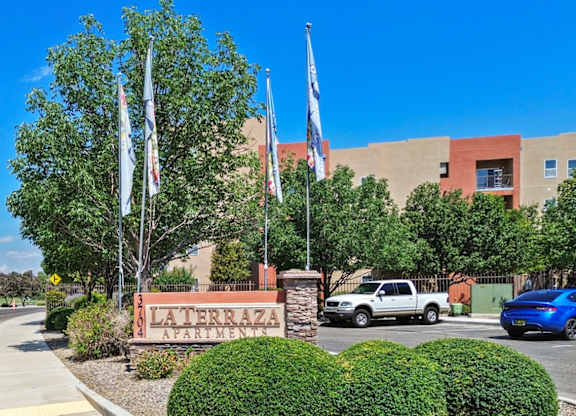 A sign for Laterza Apartments is in front of a building with trees and flags.