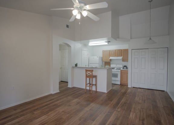 an empty living room with a kitchen and a ceiling fan