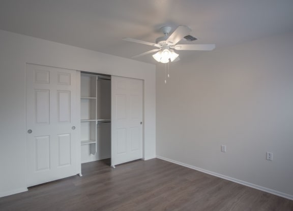 an empty bedroom with fan and closet