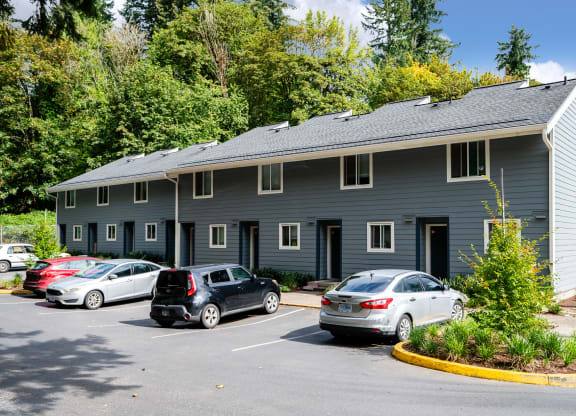 a parking lot in front of a gray building with cars parked