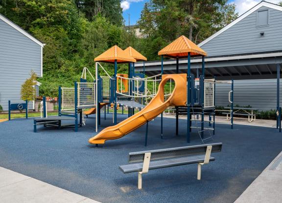 a playground with a slide and benches in front of a building
