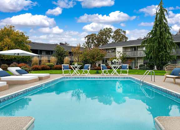 A swimming pool surrounded by lounge chairs and trees.
