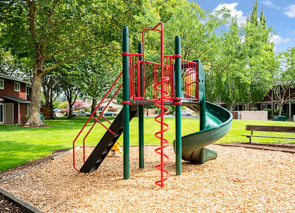 A playground with a red and green slide and a brown bench.