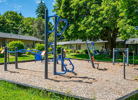 A playground with a blue swing set and a gravel ground.