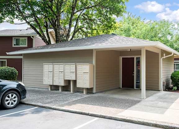 A car is parked in front of a building with a brown roof and a parking lot.