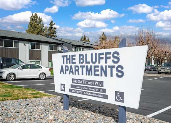A sign for The Bluffs Apartments is displayed in front of a parking lot.
